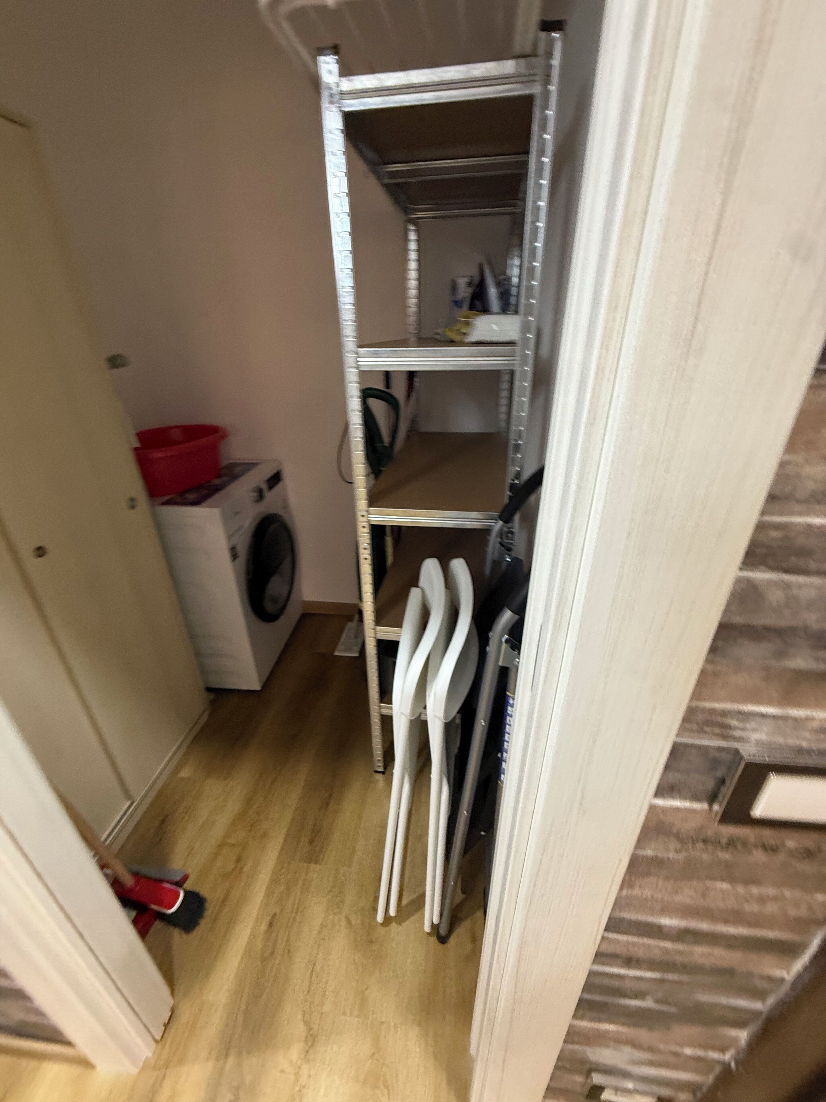 Un espace buanderie comprenant un lave-linge, des étagères et un bac rouge.
