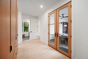 A hallway with wooden flooring, a sliding glass door with a ceiling fan, and a view of a room with a bed and a window. - Luxury Villa in Sunny Poipu with a heated pool, A/C and open floor plan. (Koloa)