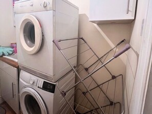 A compact laundry area with stacked washers and dryers, a metal drying rack, and a cabinet above. - Pay30nghts get up tp extra 59 free (Greater London)
