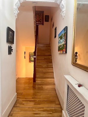 Ein Korridor mit Holzboden, einer Treppe und verschiedenen gerahmten Kunstwerken an den Wänden.