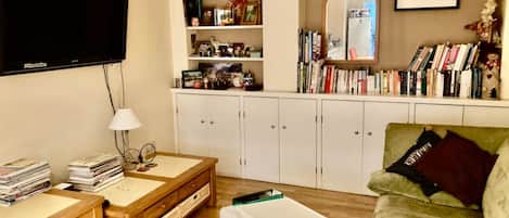 Una sala de estar con televisor, estantería, espejo y un sofá verde.