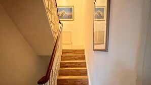 A wooden staircase with white railings and a chandelier, leading to a landing with a framed picture of a mountain. - Pay30nghts get up tp extra 59 free (Greater London)