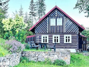 A wooden house with a steep gabled roof, a stone wall in front, and a garden with various plants. - Wellness Retreat Labská by Interhome (Spindleruv Mlyn)