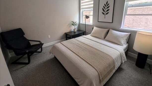 A bedroom with a bed, a chair, a nightstand, a lamp, and a window with blinds. - Breathtaking Modern Hillside Suite (San Jose)