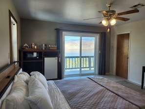 A bedroom with a bed, a desk, a refrigerator, a ceiling fan, and a view of a lake through a sliding door. - Gauche Point Guest House
Breathtaking Scenic Lake View (Mountain Mesa)