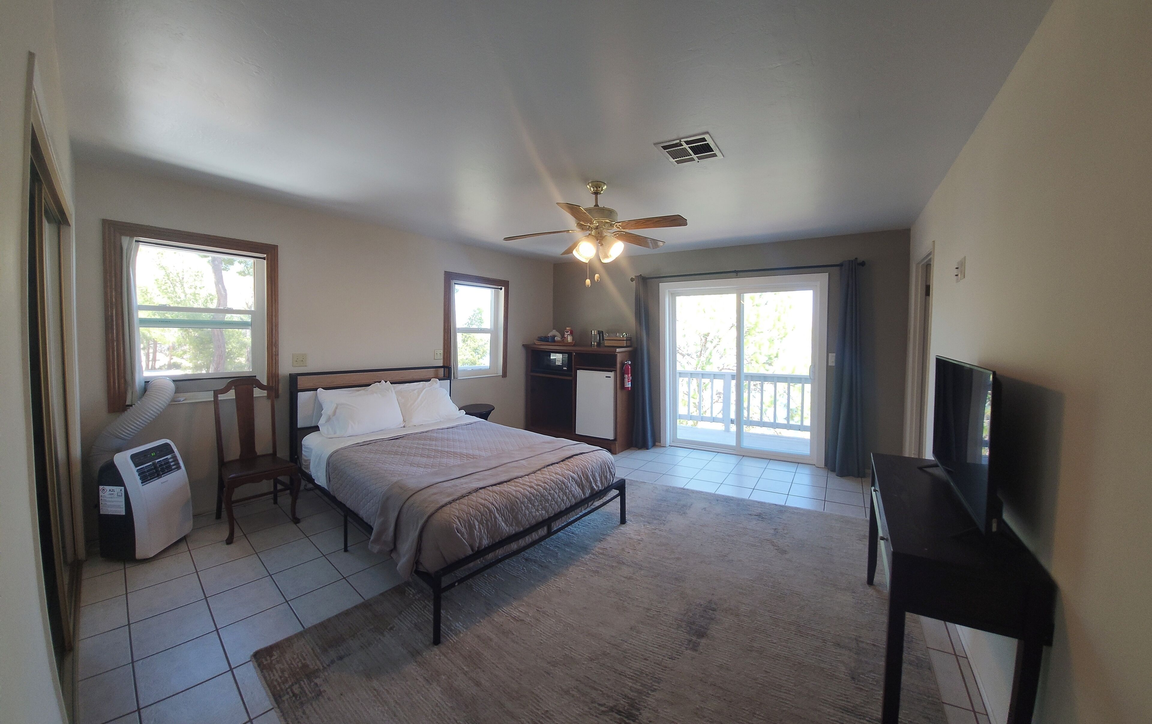 A bedroom with a bed, a desk, a television, and a ceiling fan.
