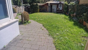 Un camino pavimentado que lleva a un área verde con un arbusto pequeño y un cobertizo al fondo.