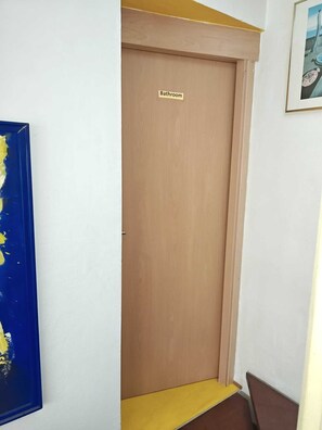 Puerta de madera cerrada con la leyenda 'Bathroom' y un escalón amarillo que lleva hasta ella.