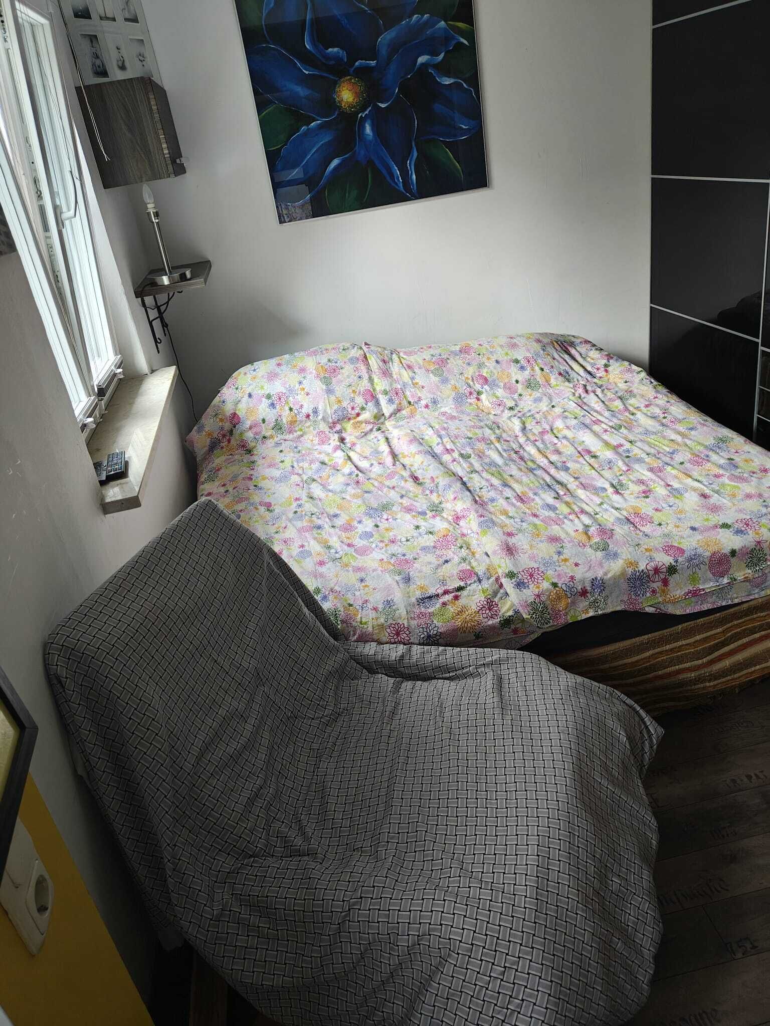 A small bedroom with a bed, a bedside table, a lamp, and a wall-mounted painting.