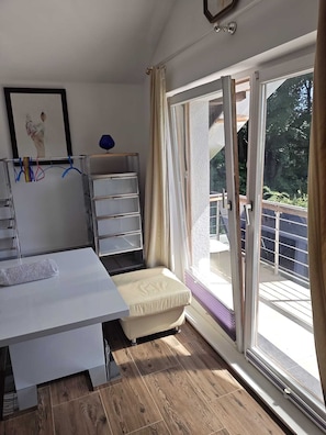 Una habitación con cama, escritorio, silla y ventana con cortinas, y vista a espacios verdes.