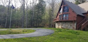 A cabin with a stone foundation, a curved driveway, and a forested backdrop. - Beautiful Modern Cabin in the woods (Daniels)