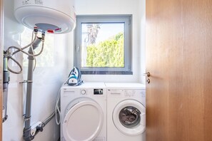 A laundry room with a washing machine, a dryer, and a window with a view of greenery. - Casa Laranja – Stunning Ocean Views & Hot Tub (Fajã da Ovelha)