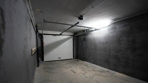 A dimly lit garage with a closed white door, concrete walls, and visible pipes. - 2-Bedroom Apartment with Mountain Views (Châtel)