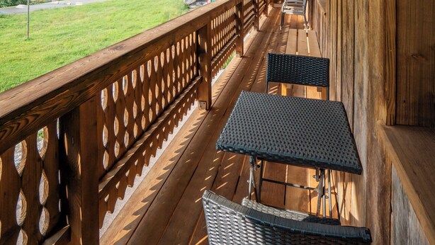 A wooden balcony with a view of a green landscape and buildings. - 2-Bedroom Apartment with Mountain Views (Châtel)