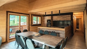 A modern kitchen with wooden cabinets, a central island, and a dining area with a table and chairs. - 2-Bedroom Apartment with Mountain Views (Châtel)