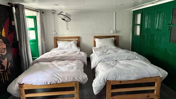 A room with two wooden beds, a green door, and a window with curtains.