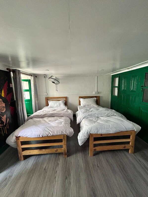 A room with two wooden beds, a green door, and a window with curtains.