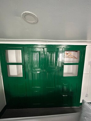 A green door with two windows and a small shelf with hangers.