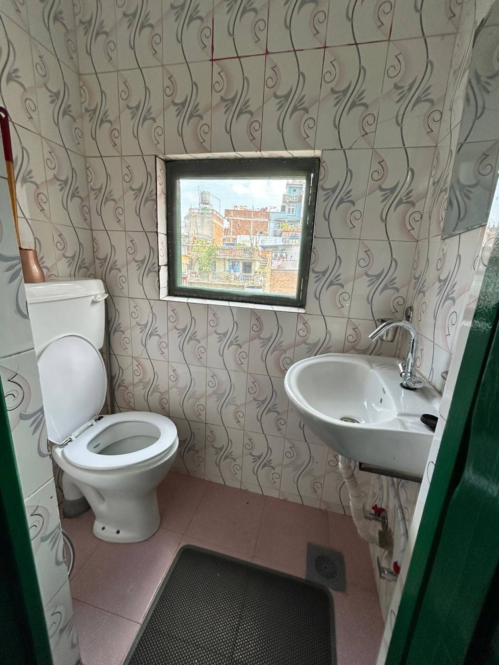 A small bathroom with a toilet, sink, and a window with a view of buildings.