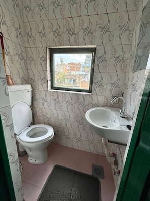 Une petite salle de bain avec des toilettes, un lavabo et une fenêtre donnant sur des immeubles.