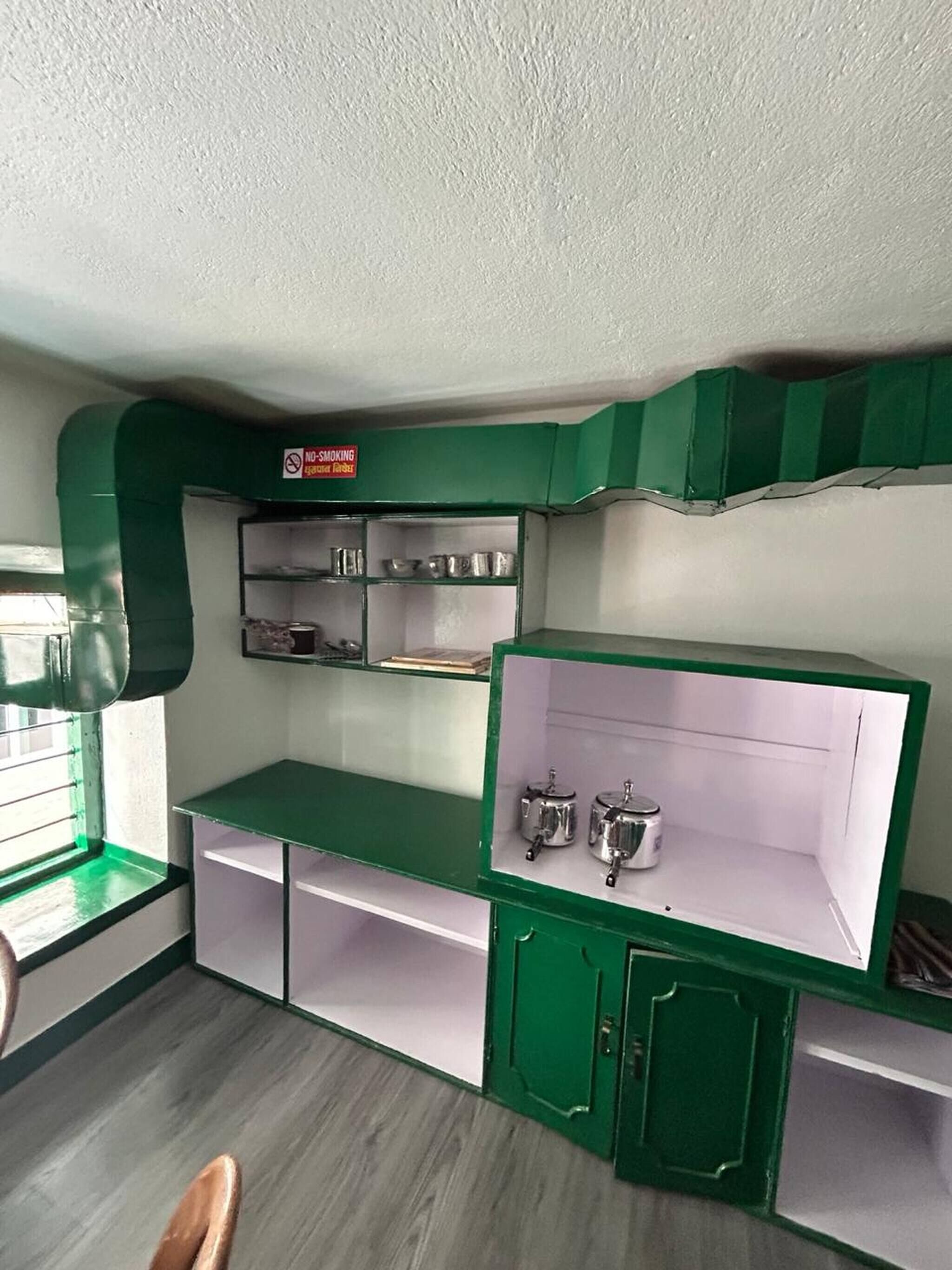 Een kamer met groene kastjes, een raam en een rookvrij bord.