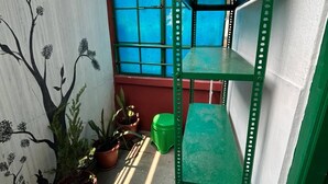 A small outdoor space with a green metal shelf, potted plants, and a wall with a tree mural.