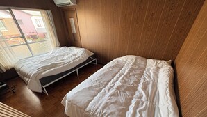 Quarto com duas camas, piso de madeira e janela com cortinas.