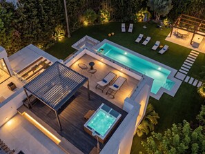 Et moderne poolområde med liggestole, jacuzzi og en træterrasse.