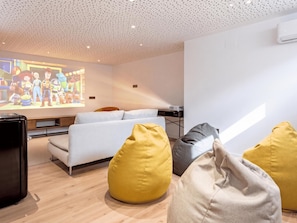 En moderne stue med en hvid sofa, gule og grå sækkestole, et fladskærms-tv og et loft med et perforeret mønster.