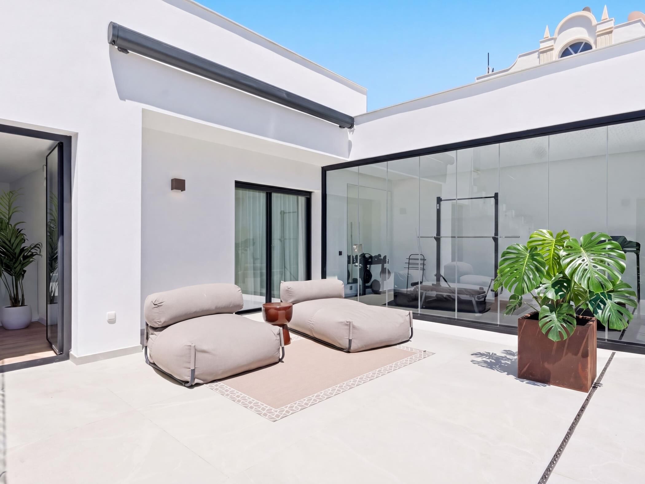 A modern outdoor living area with a glass wall, a sofa set, and a potted plant.