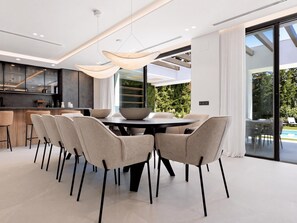 A modern dining area with a round table and six chairs, a kitchen with dark cabinetry, and a large sliding glass door leading to an outdoor area. - Villa Confort by Vacation Marbella (Estepona)