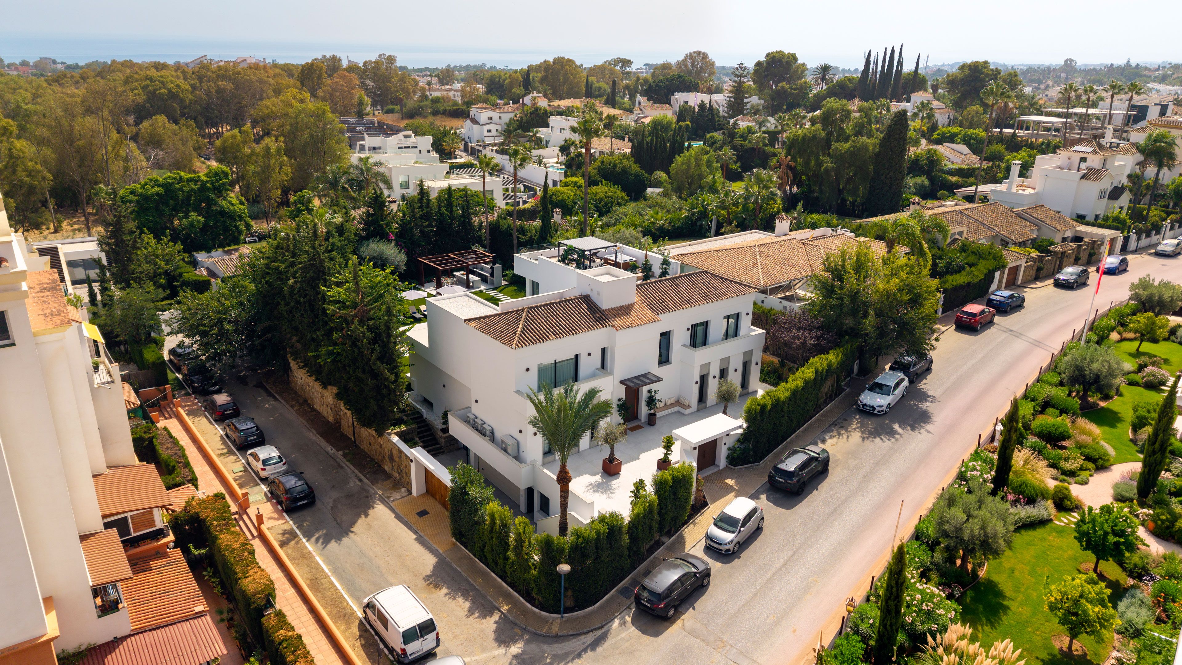 Área residencial com casas modernas, rua com carros estacionados e vegetação exuberante.