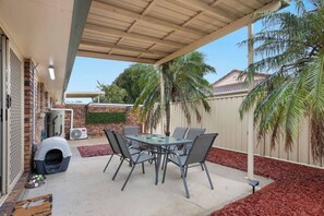 An outdoor patio with a table and chairs, a covered area, and a pet house. - Raceview Retreat…….. (Raceview)