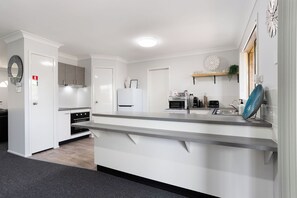 A modern kitchen with white cabinetry, a granite countertop, and stainless steel appliances. - Raceview Retreat…….. (Raceview)
