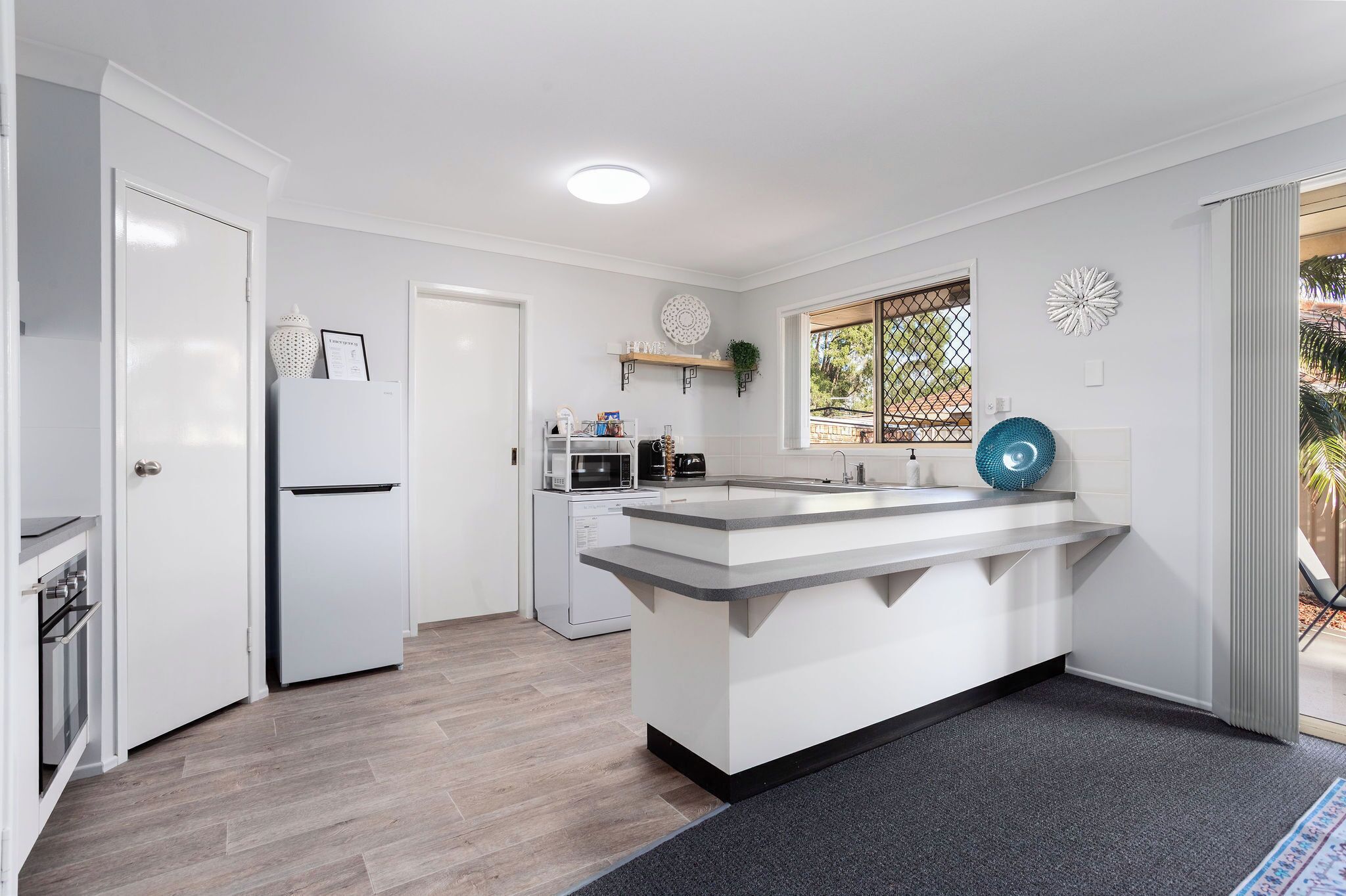 A modern kitchen with white cabinetry, a central island, a microwave, a toaster, and a window with a view of greenery.