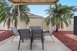 An outdoor patio with a table and chairs, surrounded by palm trees and a fence.