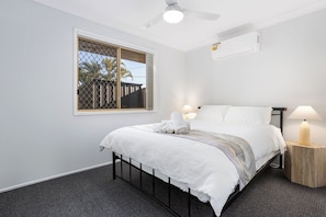 A bedroom with a bed, two bedside lamps, a ceiling fan, and a window with blinds.