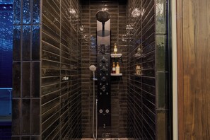 Ein modernes Badezimmer mit dunklen Fliesenwänden, einer zentralen Bedienkonsole und einem kleinen Ablagefach für Toilettenartikel.
