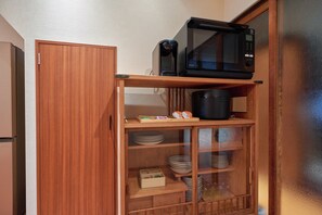 Ein Holzschrank mit einer Mikrowelle obenauf und Regalen mit Tellern und Schüsseln.