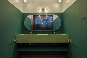 Une salle de bain avec un mur vert, un miroir rond et un lavabo doté de deux robinets.