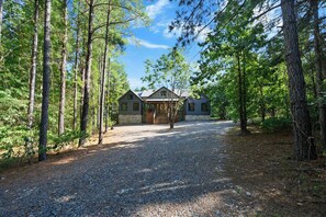A cabin with a gravel driveway, surrounded by tall trees. - Sweet Magnolia Cabin with Hot Tub and Fire Pit (Broken Bow)