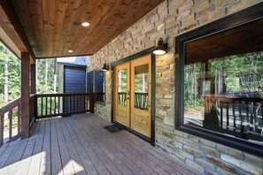 A wooden deck with stone walls and a glass door leading to an outdoor area. - Sweet Magnolia Cabin with Hot Tub and Fire Pit (Broken Bow)