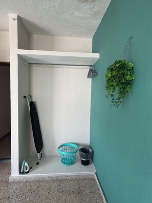 A small bathroom with a white shelf, a hanging plant, a blue basket, and a trash bin. - Casa de Familia (Puerto Vallarta)