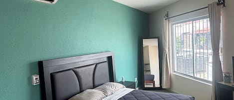 A bedroom with a bed, a ceiling fan, a window with curtains, and a wall-mounted air conditioner.