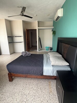A bedroom with a bed, a ceiling fan, a wall-mounted air conditioner, and a door leading to another room. - Casa de Familia (Puerto Vallarta)