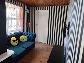 Habitación con un sofá azul, dos cojines con forma de caritas sonrientes, un extintor y una puerta con marco blanco.