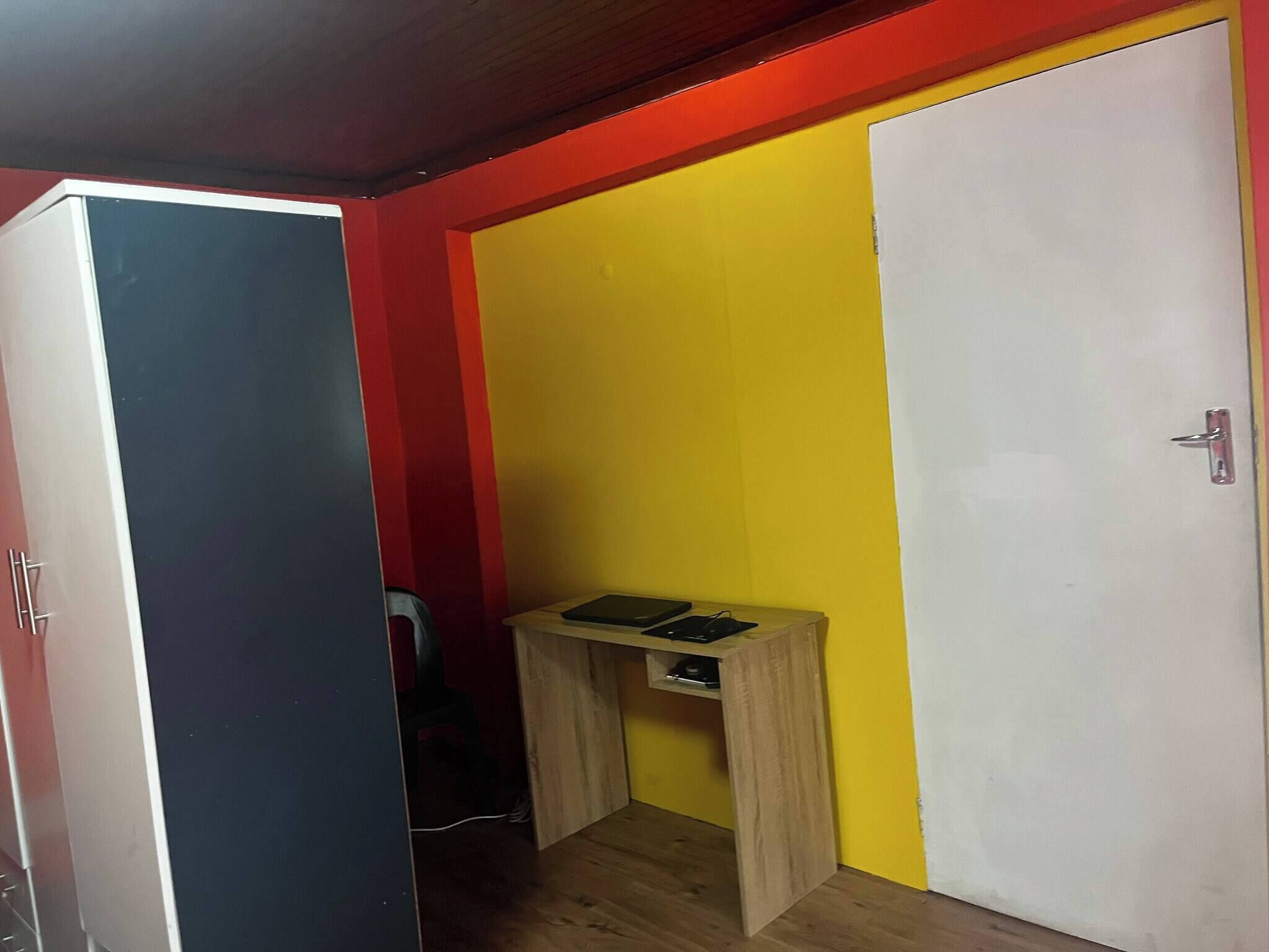 A room with a closed wardrobe, a small wooden table with two black items, and a white door.