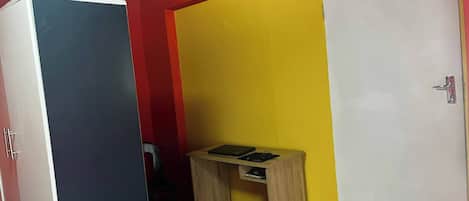 A room with a closed wardrobe, a small wooden table with two black items, and a white door.