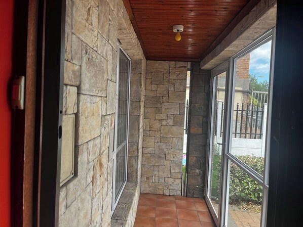 A corridor with stone walls and a tiled floor, leading to a glass door with a view of a garden. - Room-spacious House Rental With Private (Cape Town)