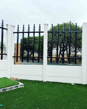 A white fence with black vertical bars and pointed tops, surrounded by green grass and trees. - Room-spacious House Rental With Private (Cape Town)